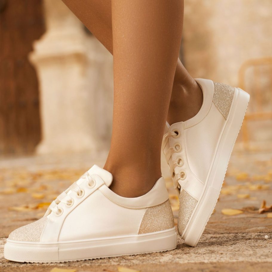 Weiße Brautsneaker mit beigem Detail, getragen von einer Person mit elegantem Bein auf einem gepflasterten Boden. Avalia Shoes Bei BAO - Waf