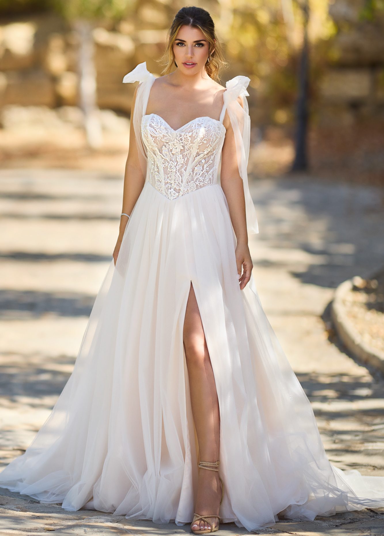 Stehende Frau trägt ein am Bein geschlitztes Prinzessinenbrautkleid und sieht glücklich in die Kamera. www.brautoutlet-warendorf.de Stehende Frau trägt ein am Bein geschlitztes Prinzessinenbrautkleid und sieht glücklich in die Kamera. www.brautoutlet-warendorf.de