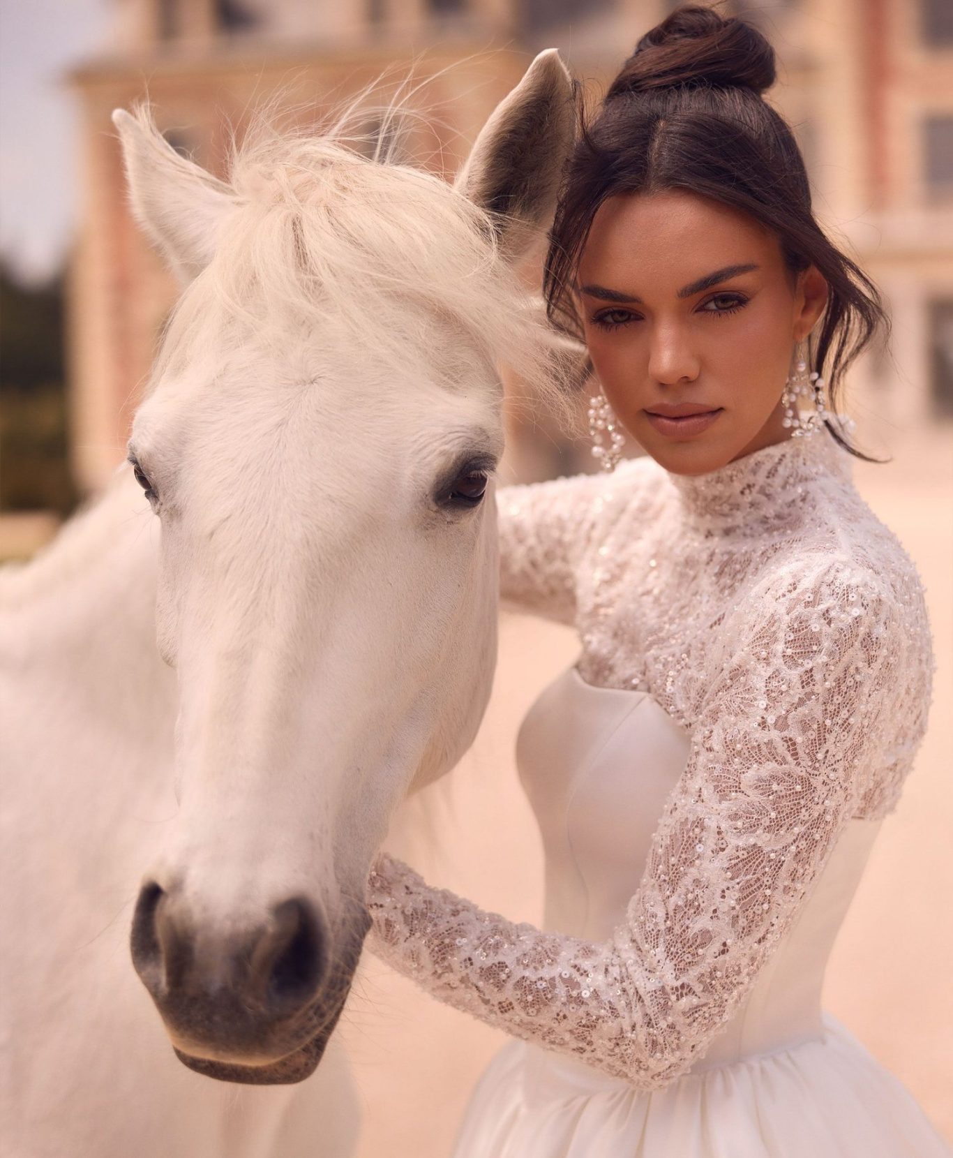 Braut mit elegantem Pferd vor einem Schloss, sie trägt  ein perlenbesticktes Brautkleid BAO Warendorf, www.brautoutlet-warendorf.de