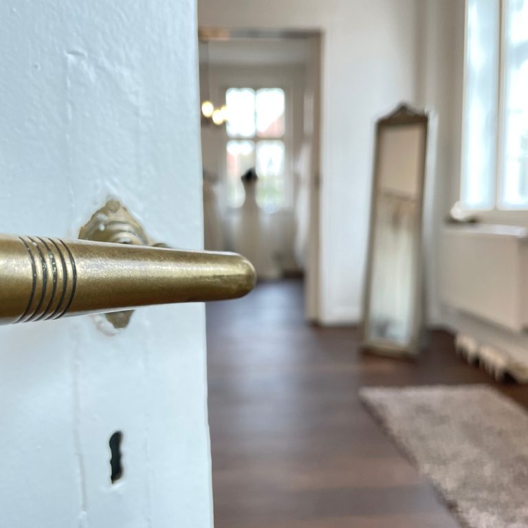 Goldener Türgriff mit Blick auf einen hellen Raum im Braut Outlet Warendorf. Hier findest Du Dein Brautkleid zum Outletpreis. BAO www.brautoutlet-warendorf.de Goldener Türgriff mit Blick auf einen hellen Raum im Braut Outlet Warendorf. Hier findest Du Dein Brautkleid zum Outletpreis. BAO