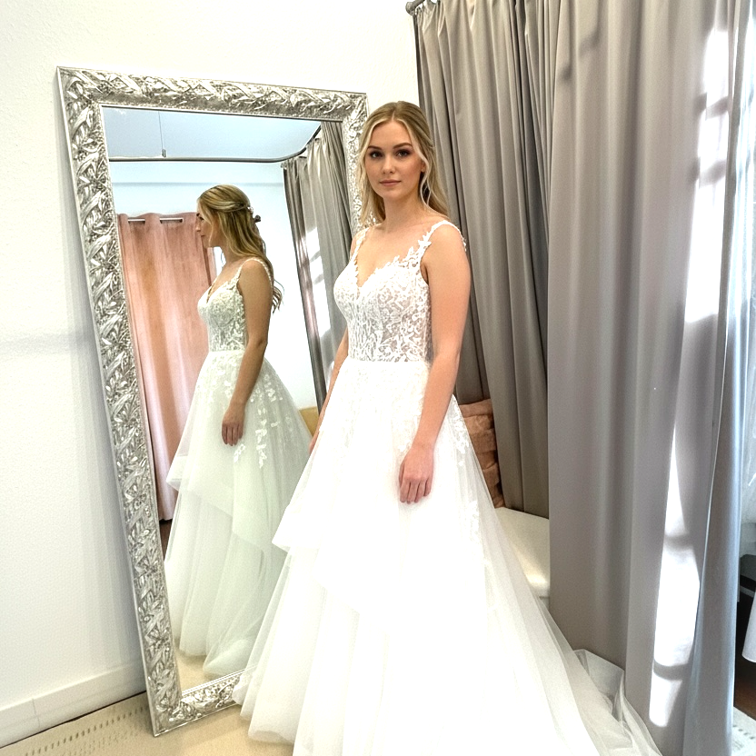 Braut in einem eleganten weißen Kleid steht vor einem Spiegel im Braut Outlet Warendorf. Persönliche Beratung. BAO