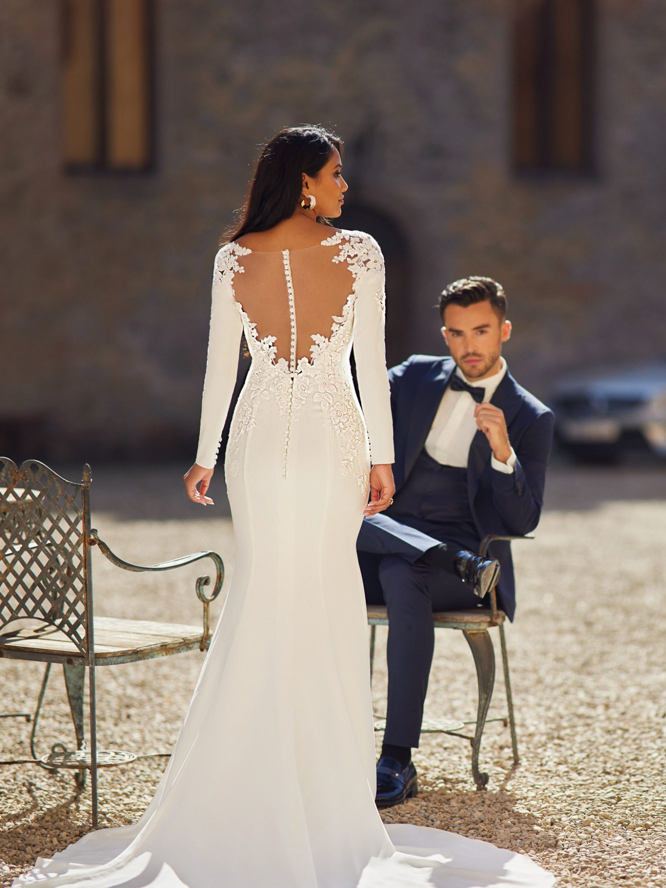 Brautpaar, er sitzt und sieht in die kamera, sie steht mit dem Rücken, mit Herzausschnitt und sieht zu Ihm. BAO Braut Outlet warendorf, www.brautoutlet-warendorf.de Brautpaar, er sitzt und sieht in die kamera, sie steht mit dem Rücken, mit Herzausschnitt und sieht zu Ihm. BAO Braut Outlet warendorf, www.